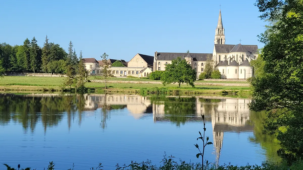 Les bâtiments de l’abbaye et son clocher, reflétés dans l’eau de l’étang sous un ciel bleu