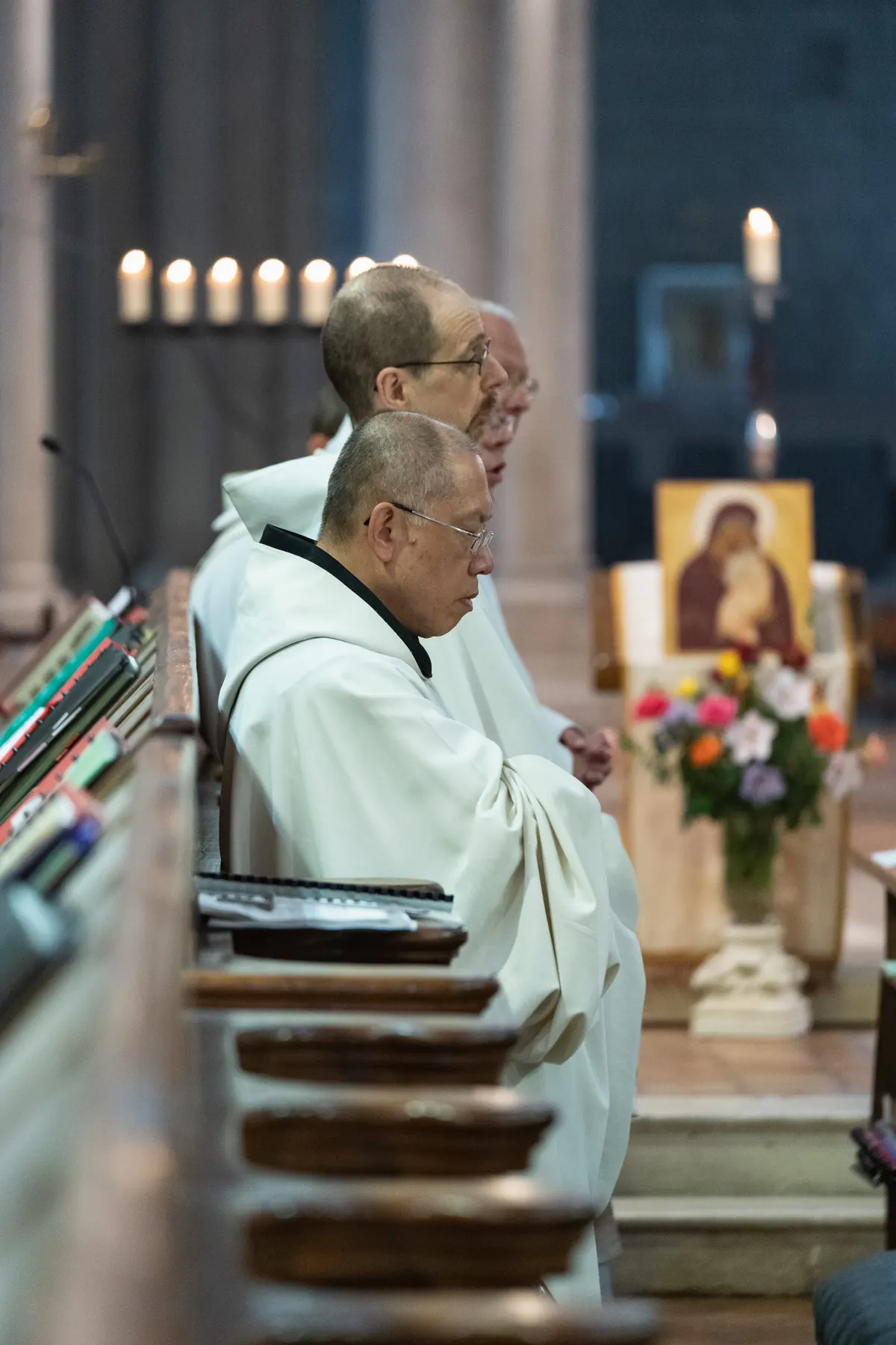 Les moines chantent, livres ouverts, près d’une icône de la Vierge fleurie