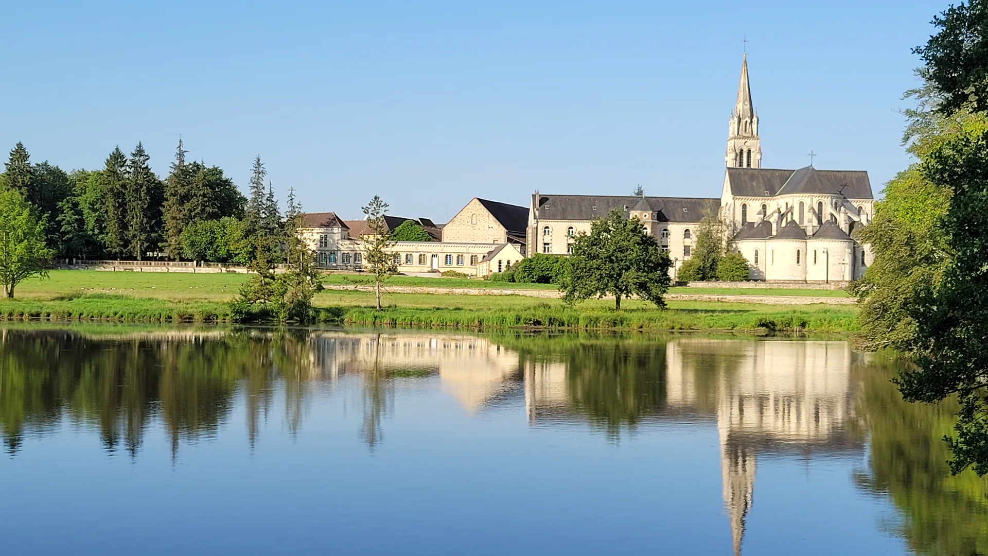 L’abbaye et son clocher se reflétant dans l’étang, un matin d’été