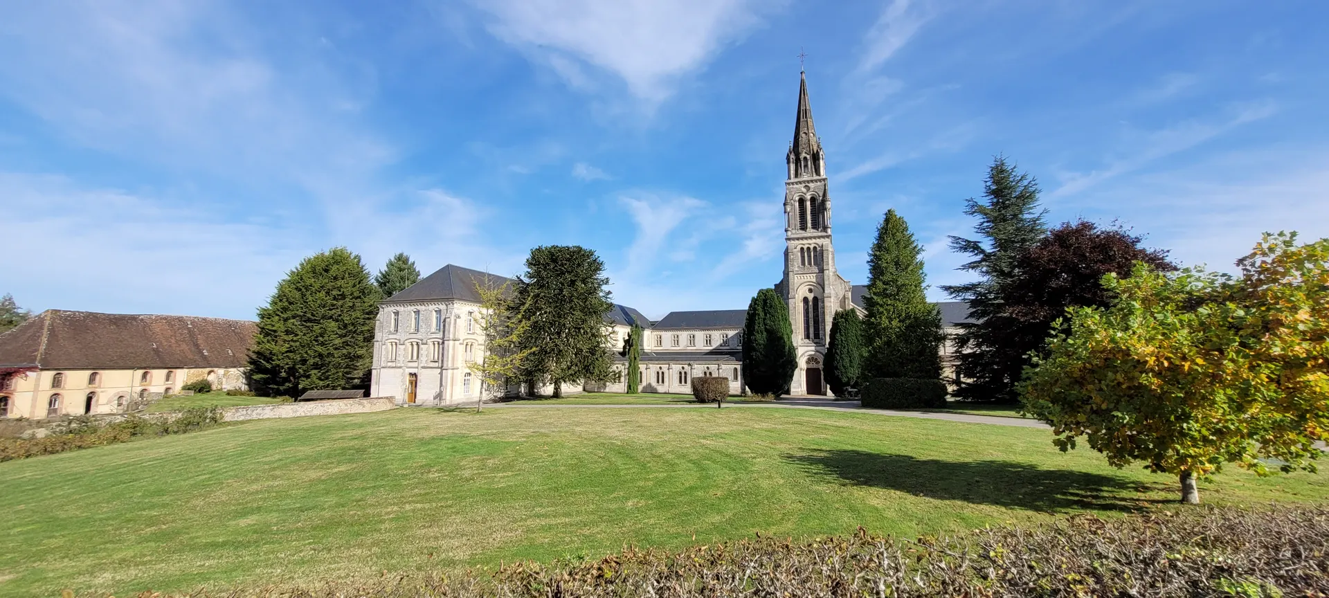 L’abbaye vue du parc : la façade, le clocher de l’église et les grands arbres sous un ciel bleu